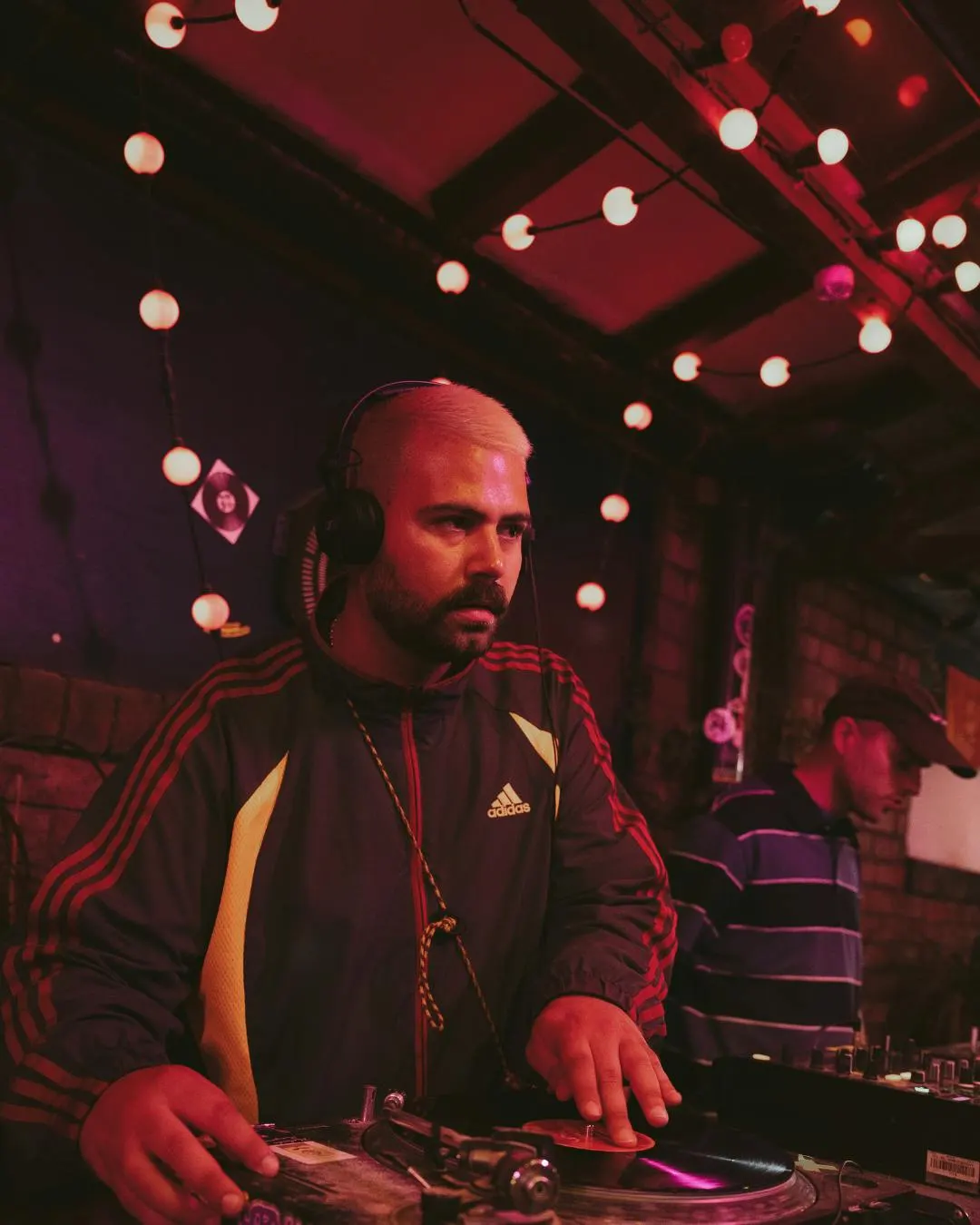 DJ performing at a turntable under red and white pendant lights in a nightclub setting.
