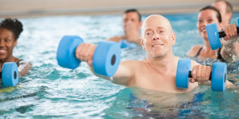 Group of adults exercising in a swimming pool with blue foam dumbbells during an aquatic fitness class.