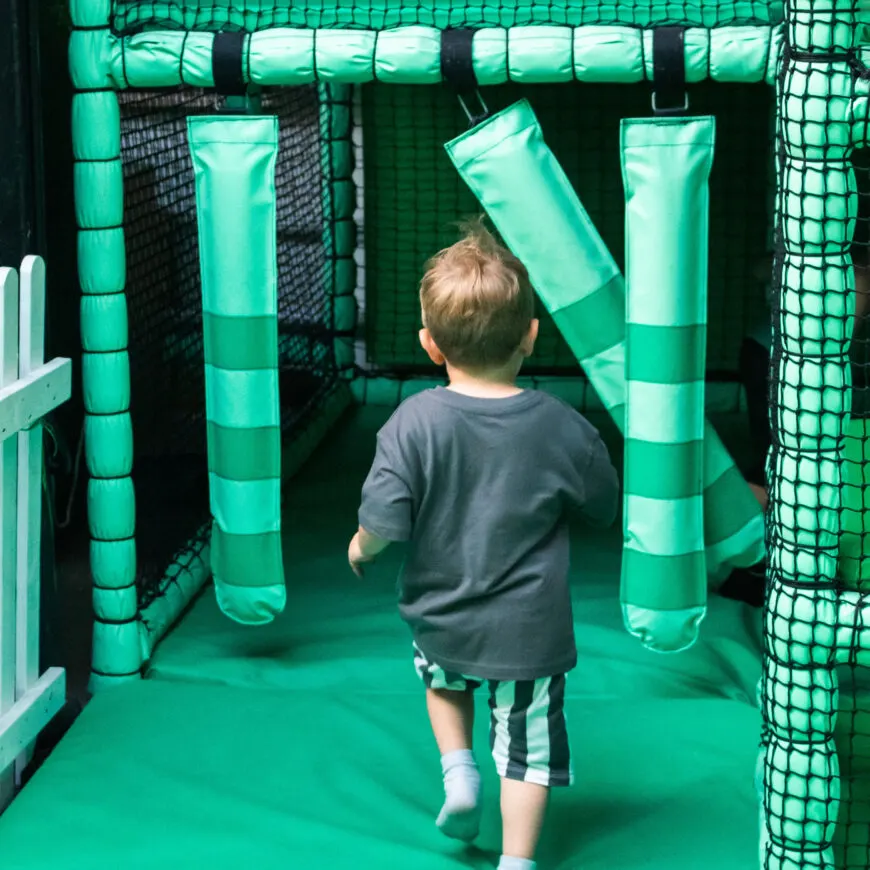 A young child running through a green inflatable tunnel obstacle course with mesh netting sides.