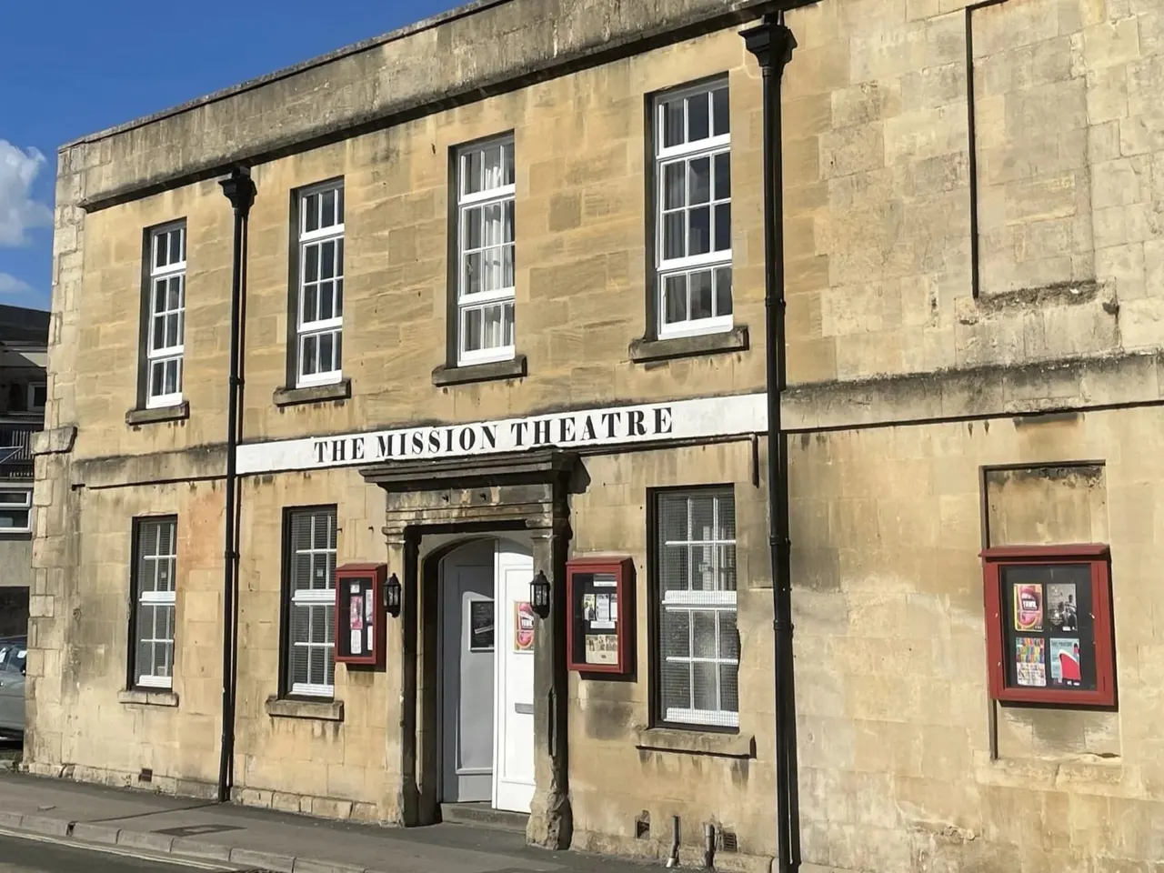 Historic stone theatre building with cream-coloured façade, white-framed windows, red poster cases, and central entrance beneath a signboard.