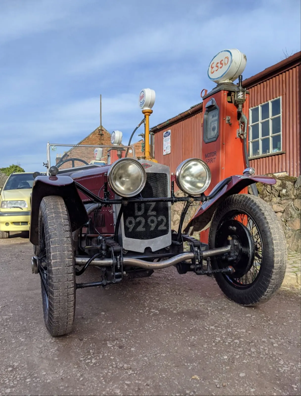 Vintage maroon and red motor vehicles with Esso pump signs displayed at an outdoor leisure venue.