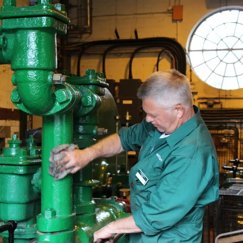 Man in green work jacket inspecting large green industrial machinery in a heritage engineering workshop.