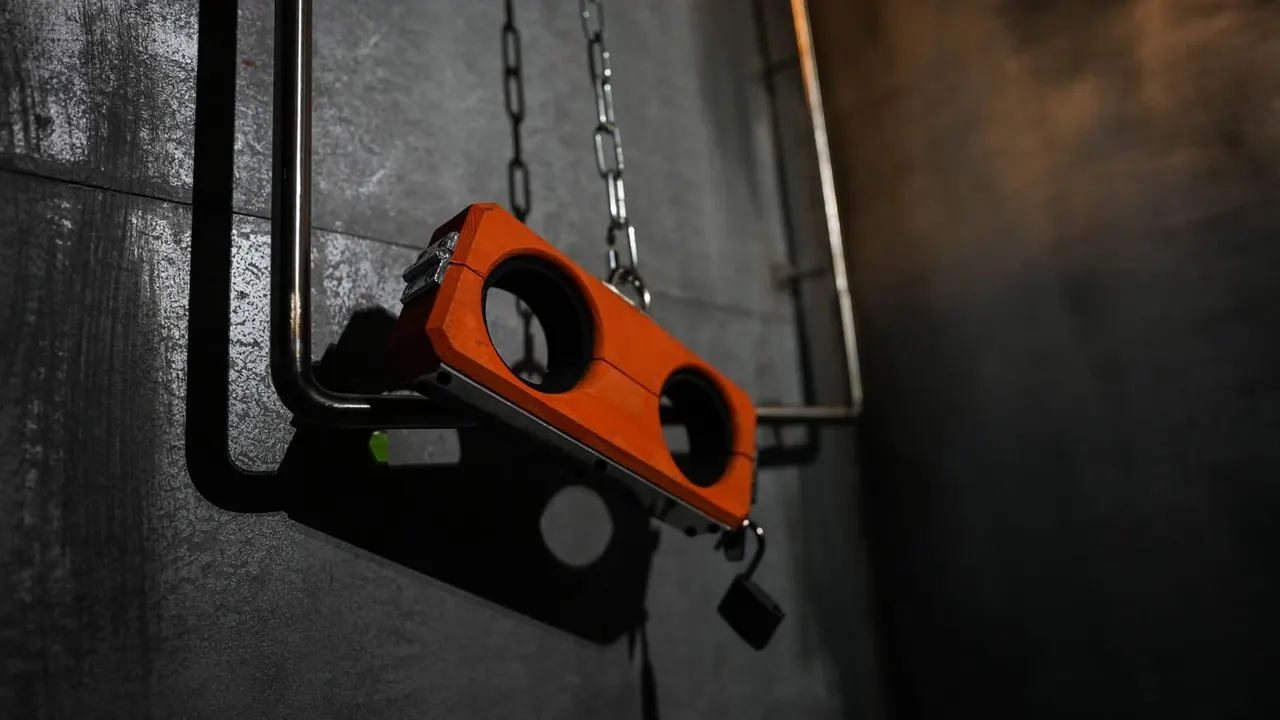 An orange and black boxing punch bag hanging from chains in a dark room with concrete walls.
