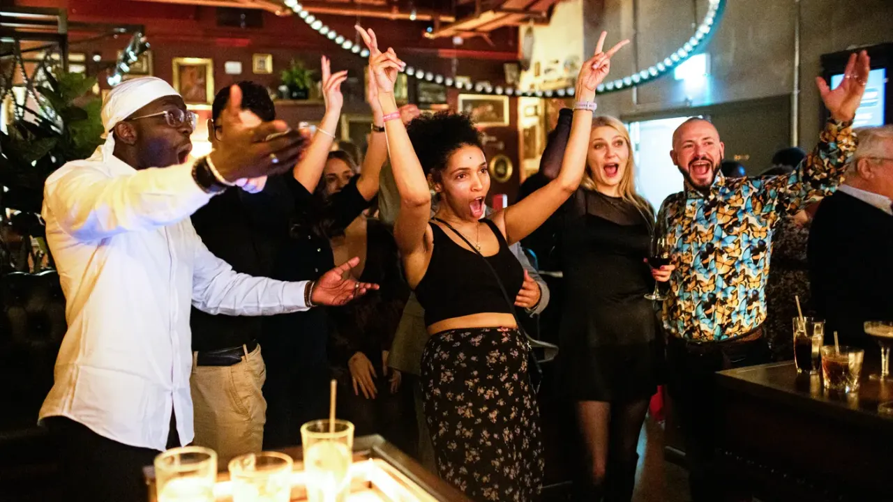 A group of people celebrating and dancing together at an indoor venue with string lights and decorated walls.