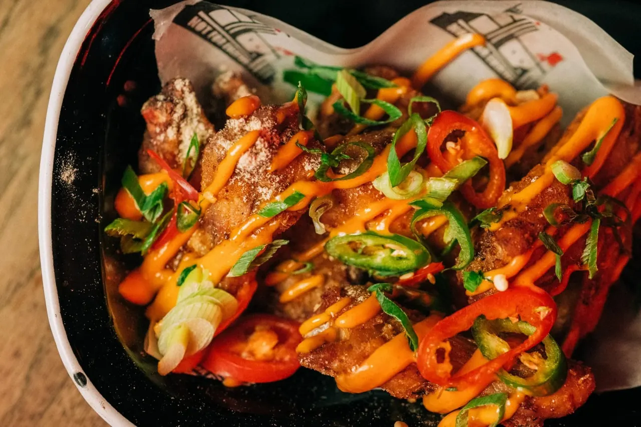 Fried meat strips topped with sliced chillies and spring onions on a black plate.