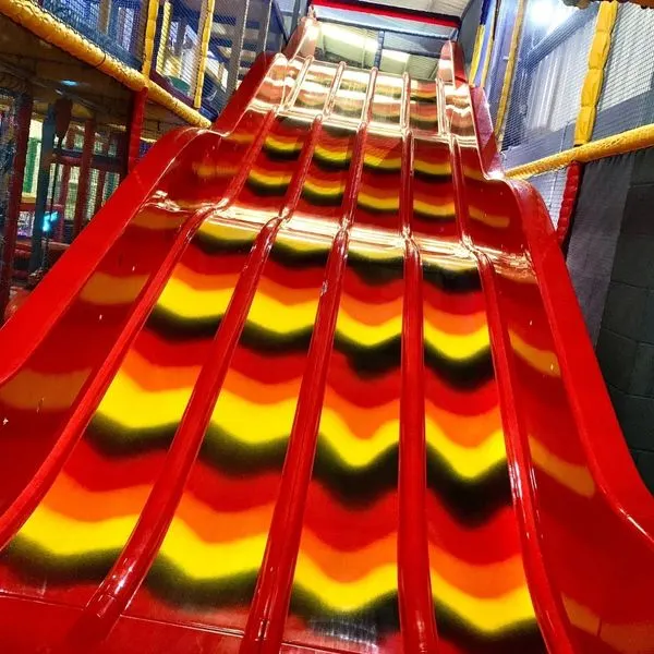 Bright red inflatable slide with yellow sections inside an indoor play centre.