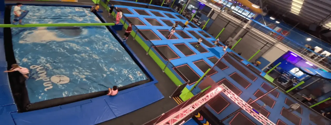 Children playing in an indoor trampoline park with a foam pit and climbing wall structures.