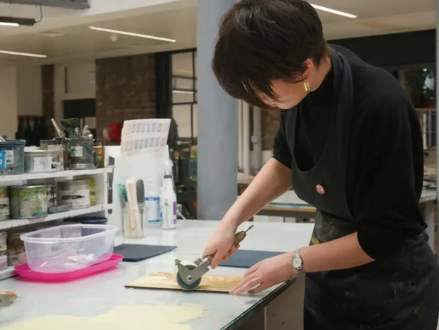 Person using a printing press tool at a workbench in a printmaking studio.