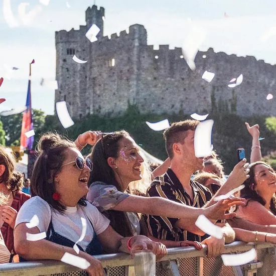 Visitors throwing white confetti in the air at an outdoor event in front of a medieval stone castle.
