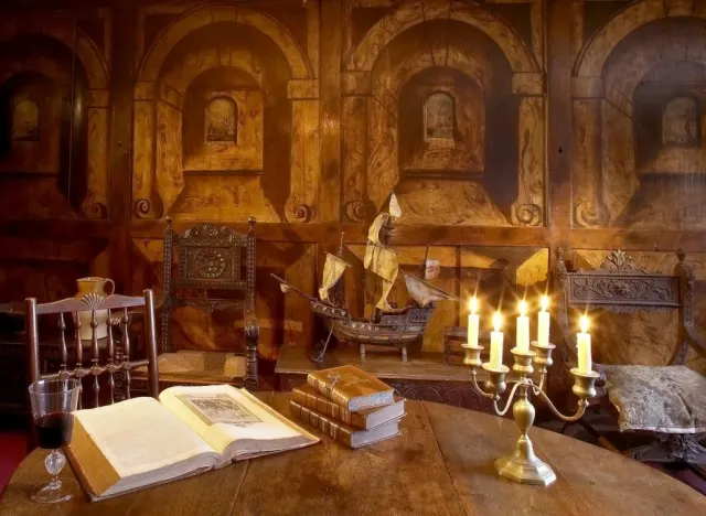 Interior display of a historic room with an open book, candlestick, and period furnishings against ornate painted walls.