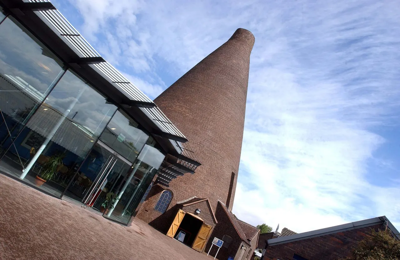 Tall brick chimney and modern glass-fronted building with blue sky above.