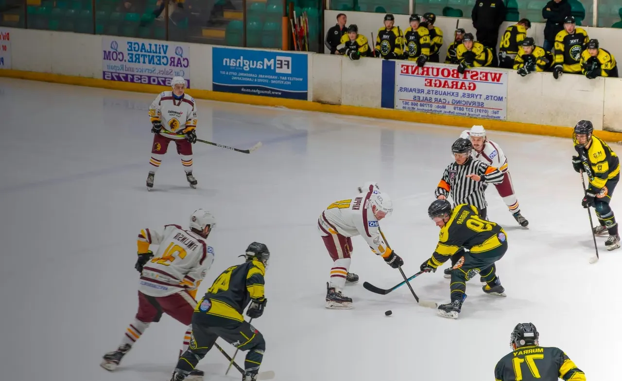 Ice hockey match in progress with players in maroon and gold versus black and yellow jerseys competing for the puck.