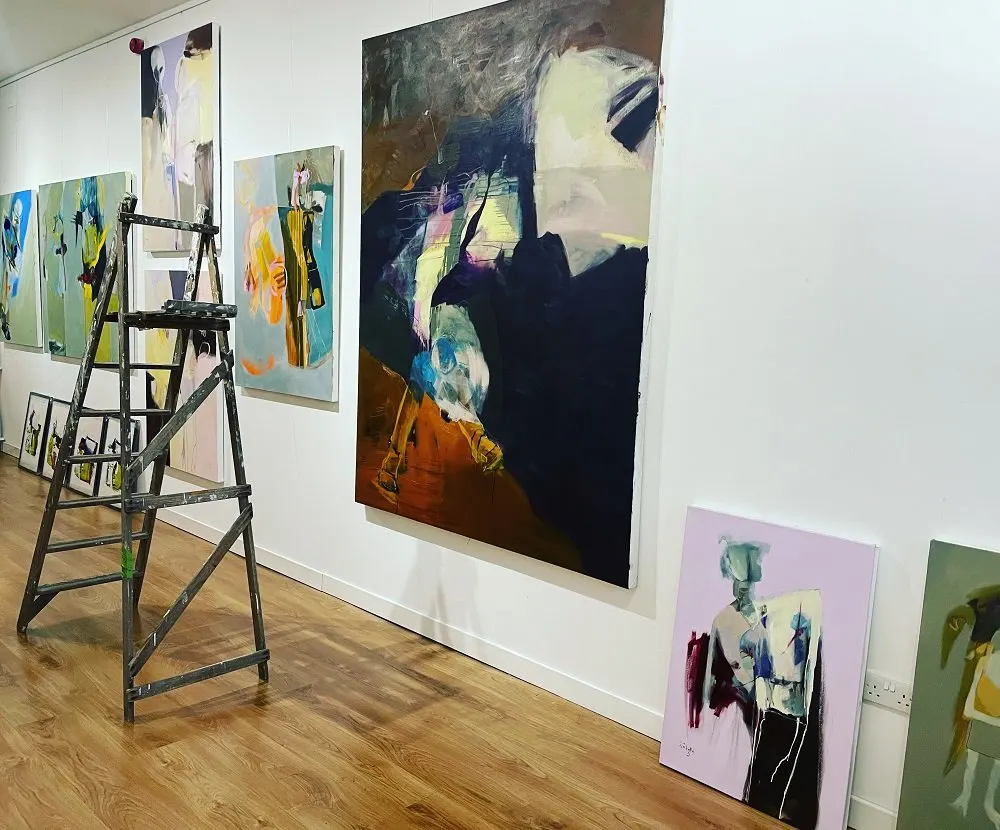 Art gallery interior with abstract paintings on walls and a stepladder on wooden flooring.