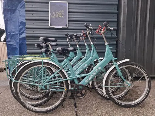 Row of turquoise hire bicycles lined up against a dark corrugated metal building.