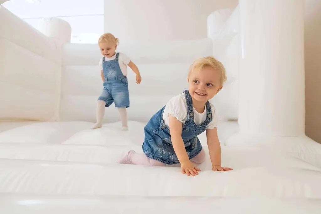 Two young children playing inside a white inflatable bouncy castle.