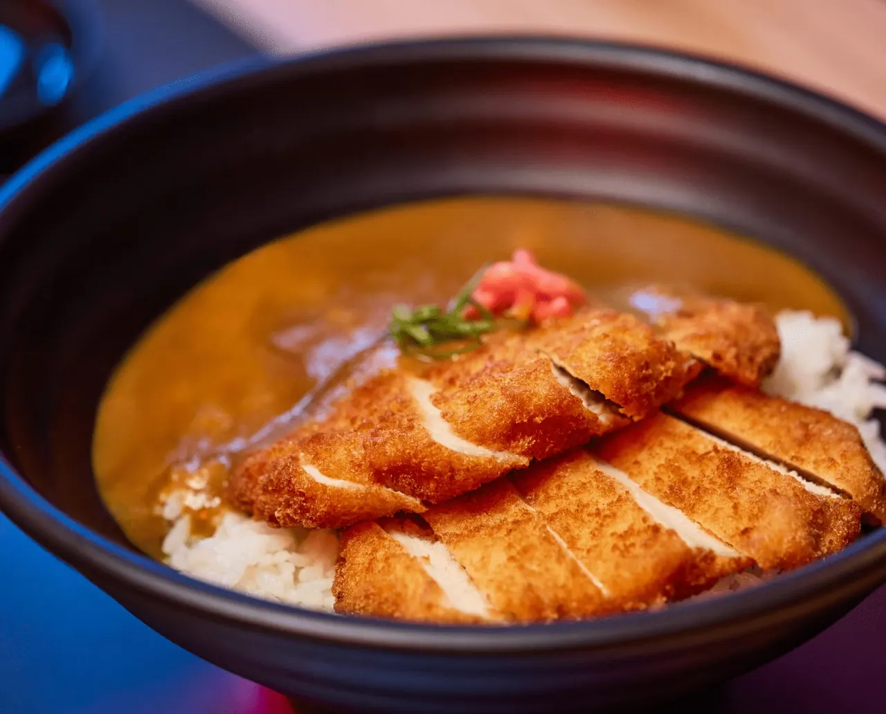 Crispy fried tofu slices in golden broth with garnish, served in a dark bowl.