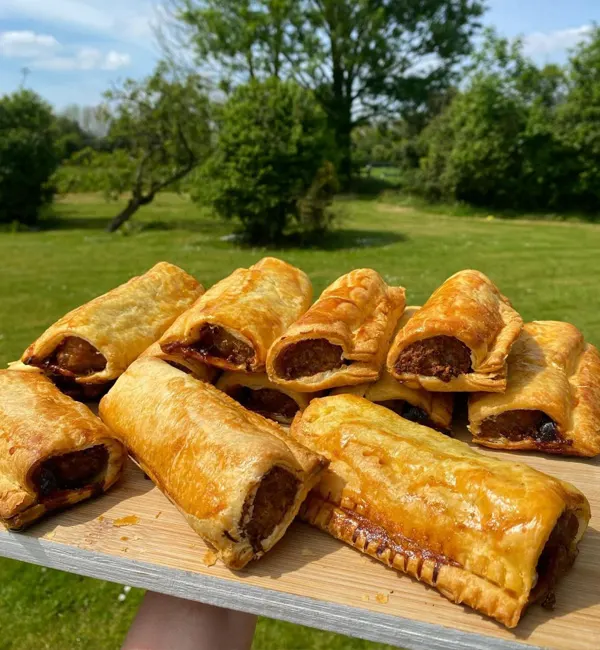 Golden baked sausage rolls arranged on a wooden board in a sunny garden setting.