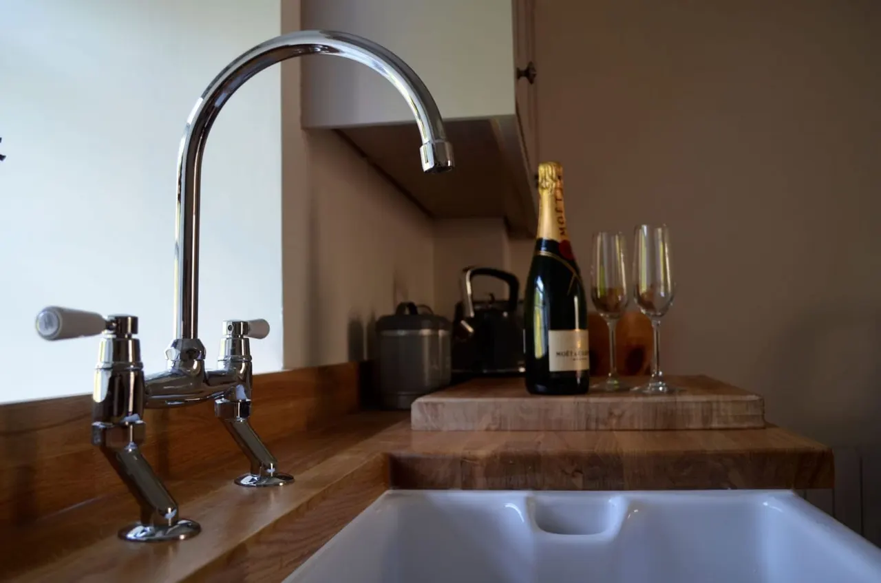 Luxury kitchen sink with chrome tap, champagne bottle and glasses displayed on wooden counter beside basin.