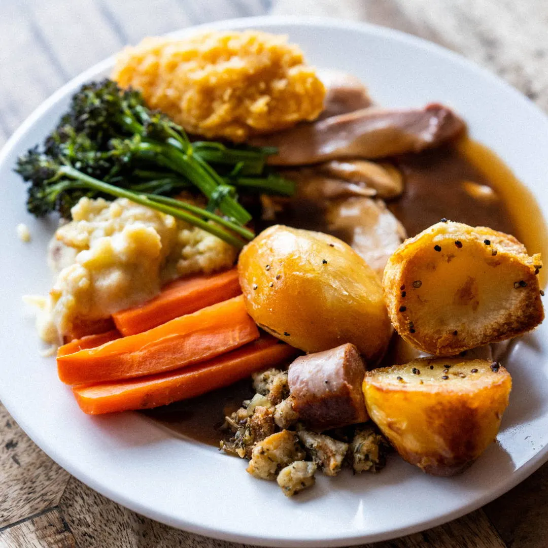 Roasted dinner plate with meat, roasted potatoes, carrots, greens, stuffing and gravy.