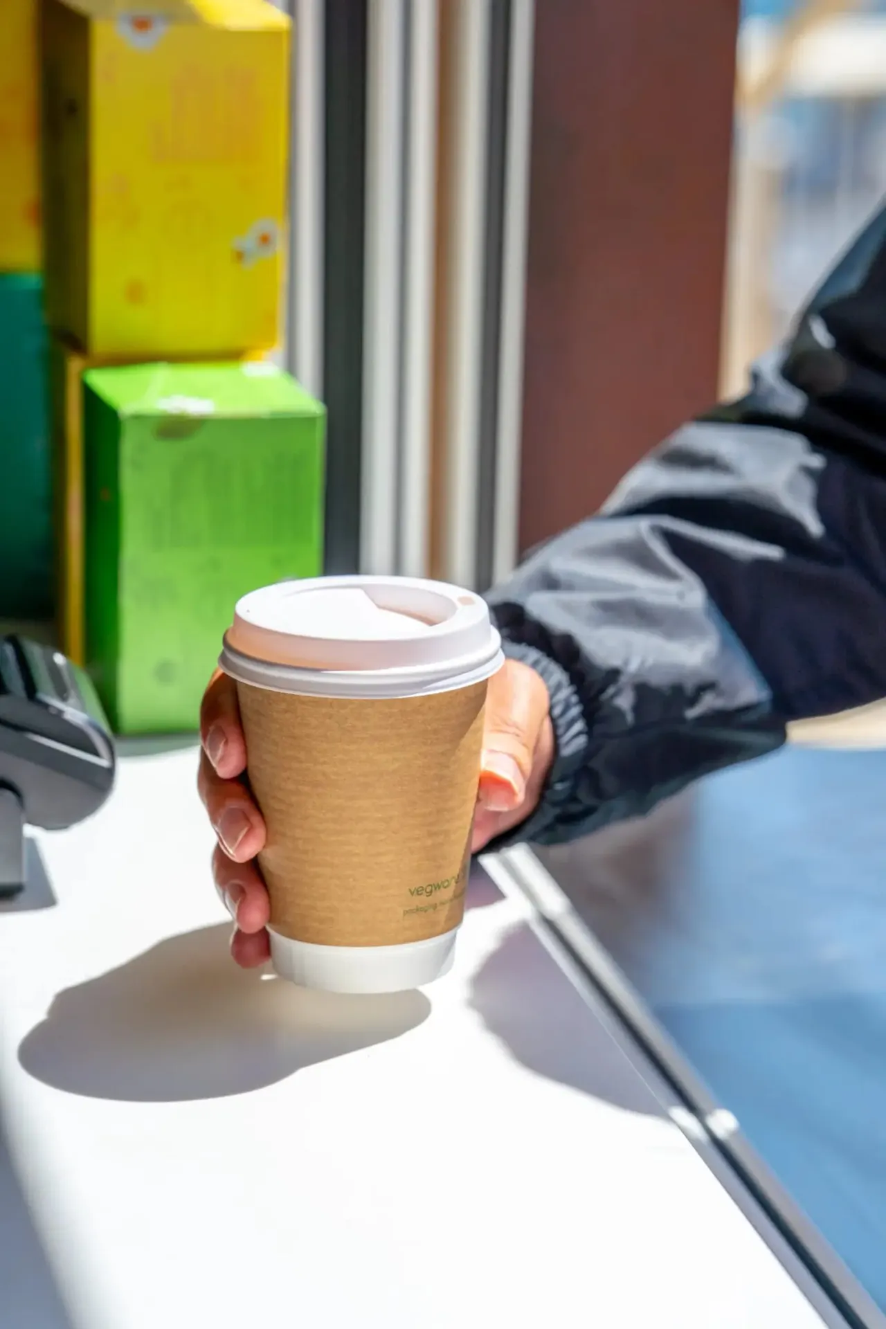 Person holding a takeaway coffee cup with cardboard sleeve at an outdoor leisure venue.