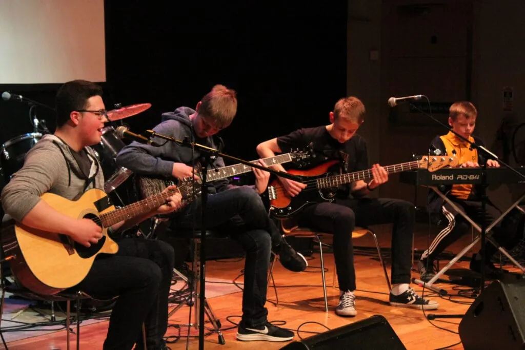 Four young musicians performing together on stage with guitars and keyboards.
