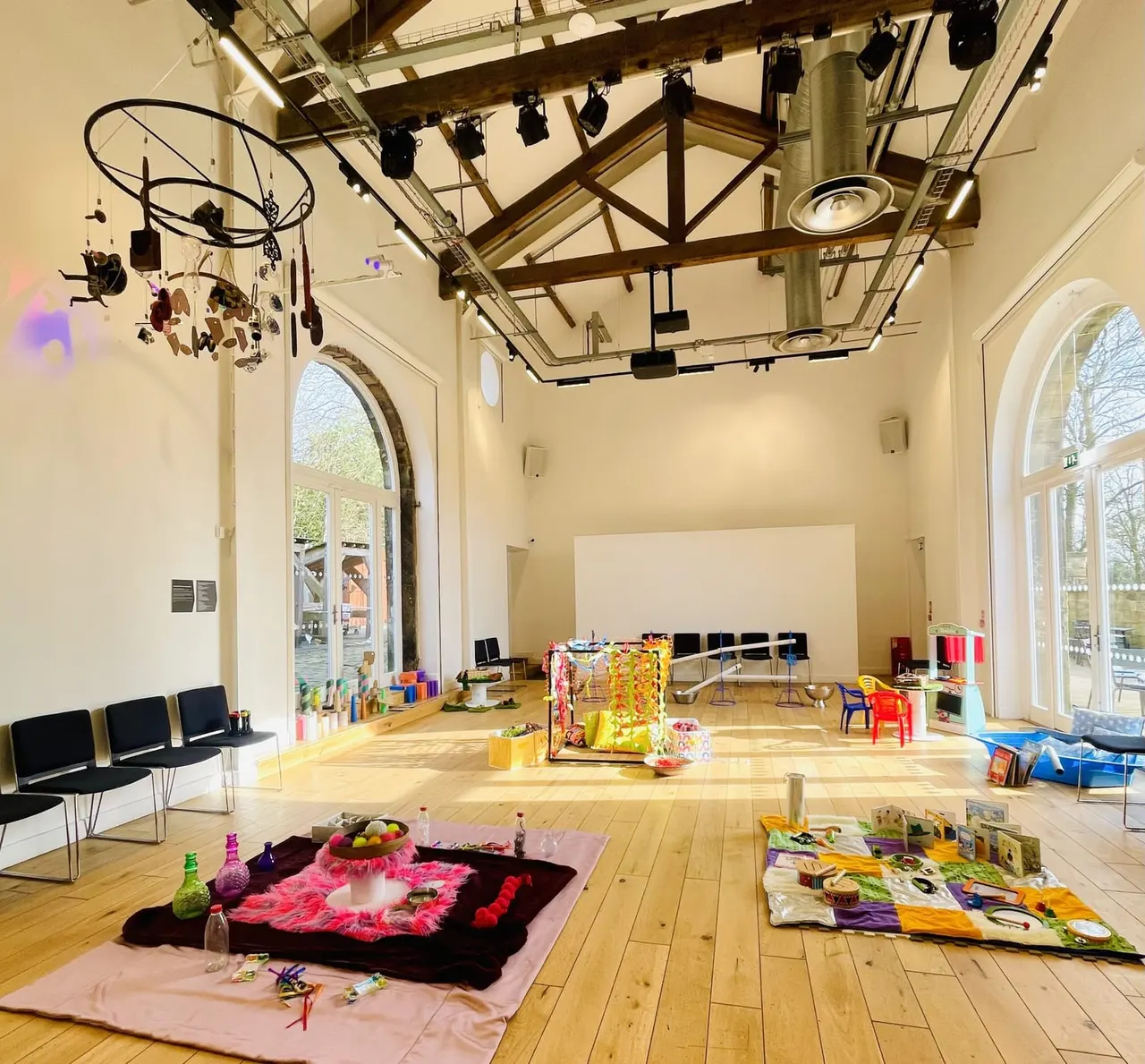 Spacious art studio and creative activity space with wooden beams, large windows, art supplies, and colourful materials laid out on the floor for interactive workshops.