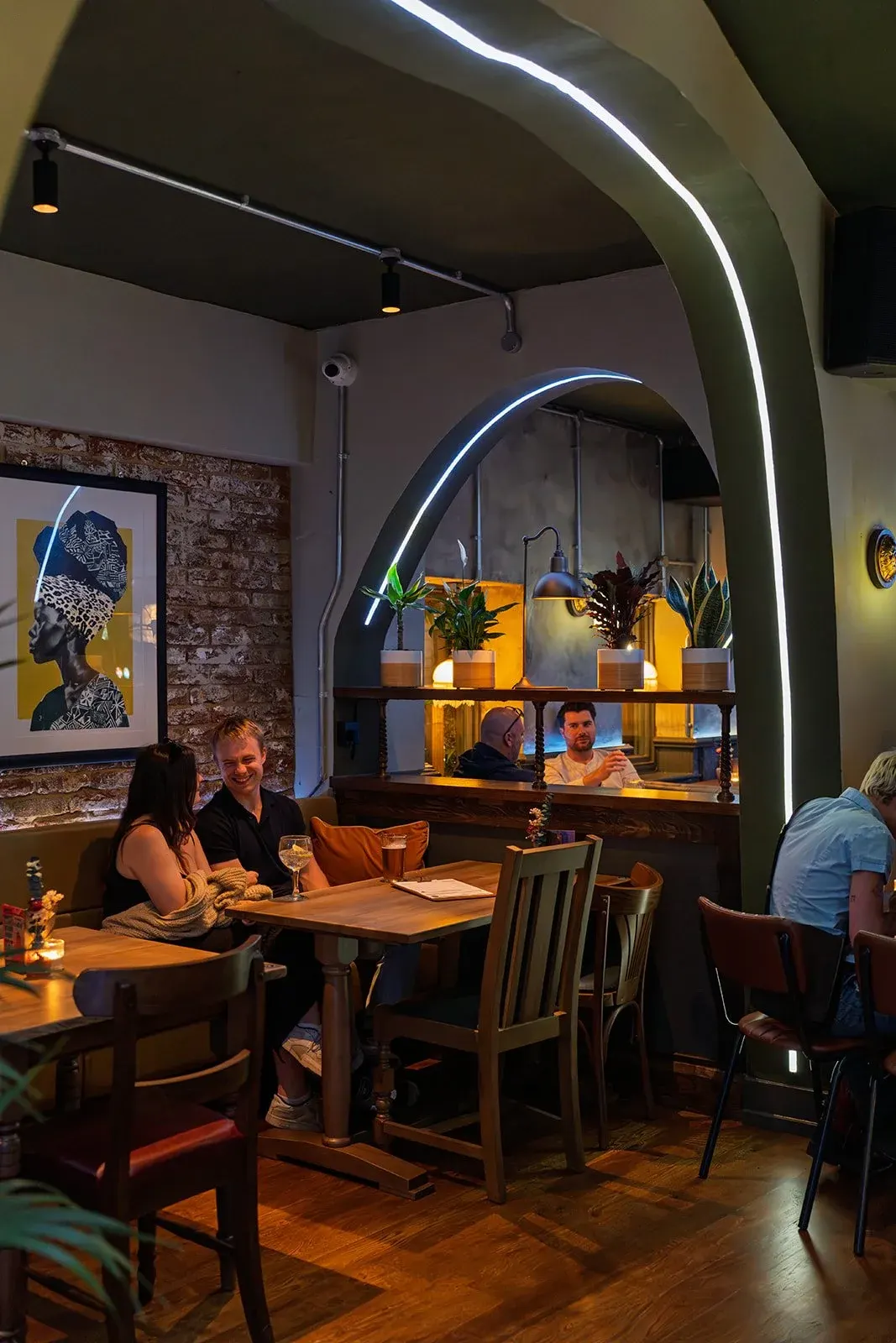 Diners seated at tables in a modern restaurant interior with neon-lit architectural features and exposed brick walls.