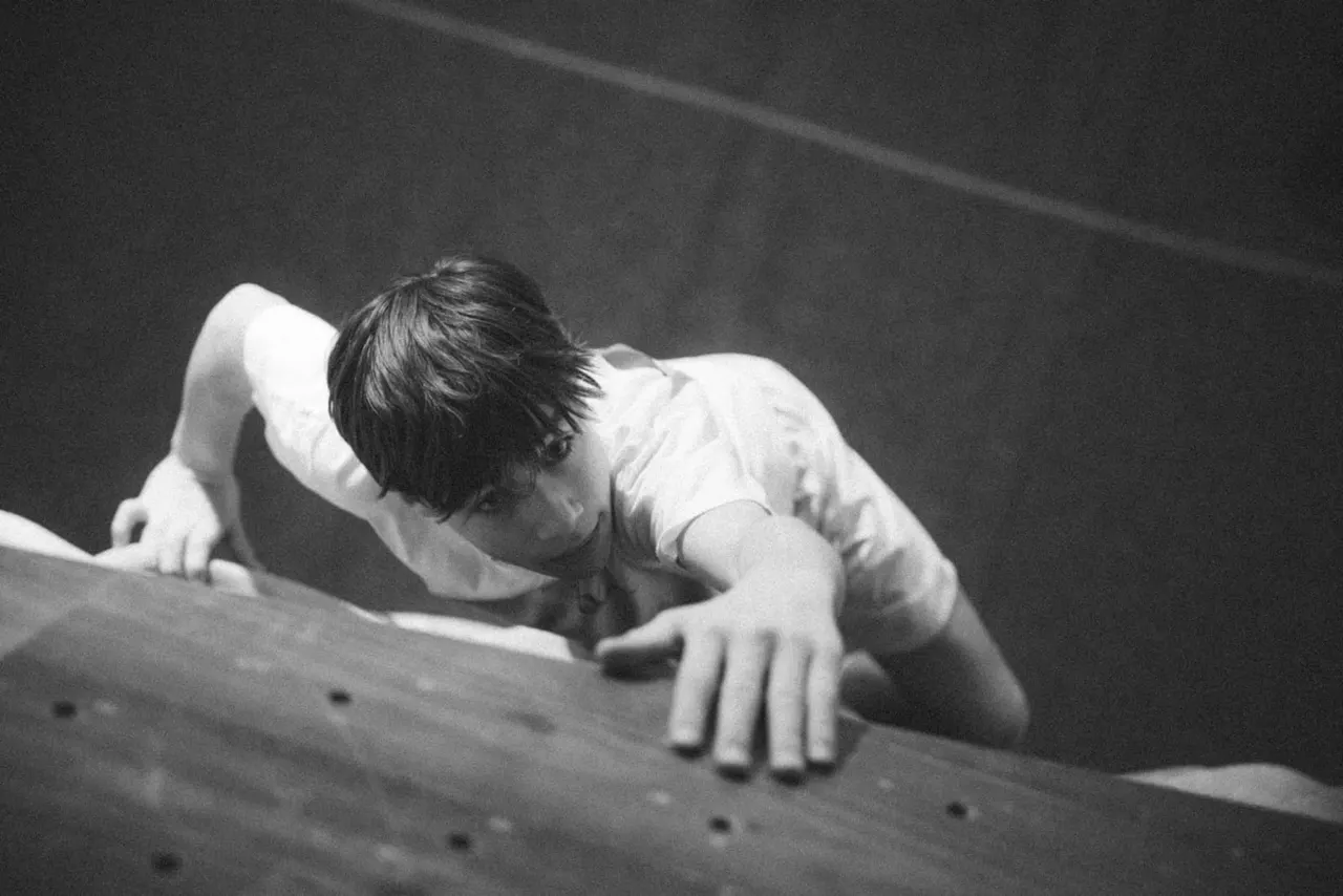 Child climbing an indoor rock wall with handholds, concentrating on their grip.