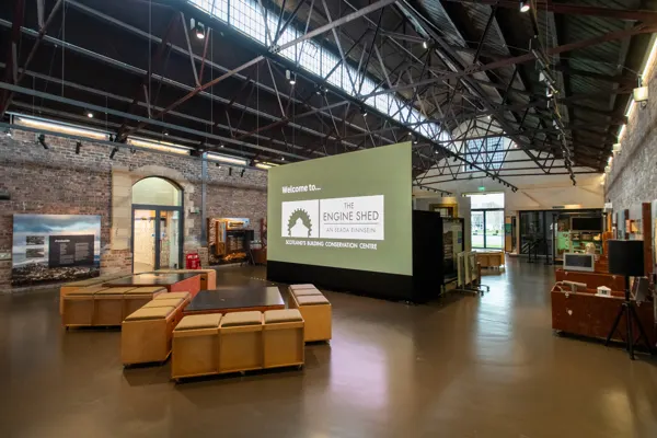 Interior of a modern museum gallery with high ceilings, brick walls, exhibition displays and seating areas.