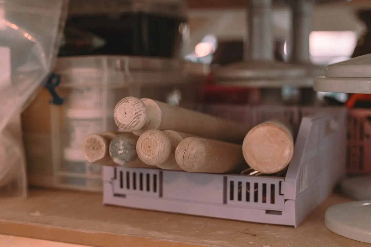 Wooden dowels and craft materials arranged in a storage tray at a pottery workshop.
