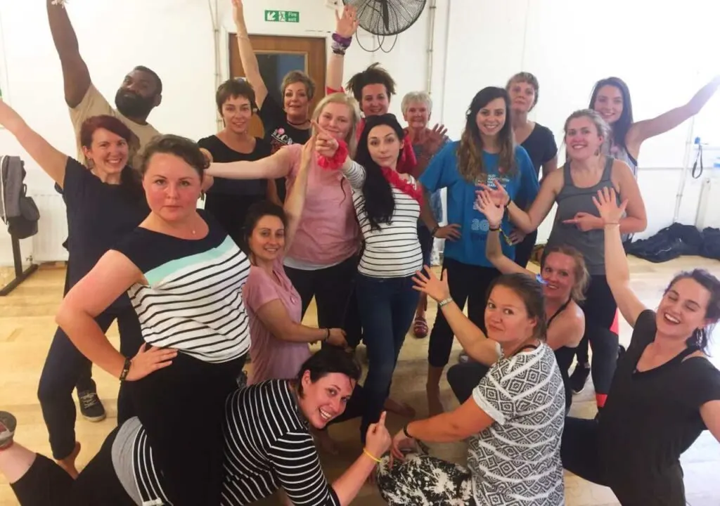 A large group of people posing together cheerfully in a wooden-floored dance studio.