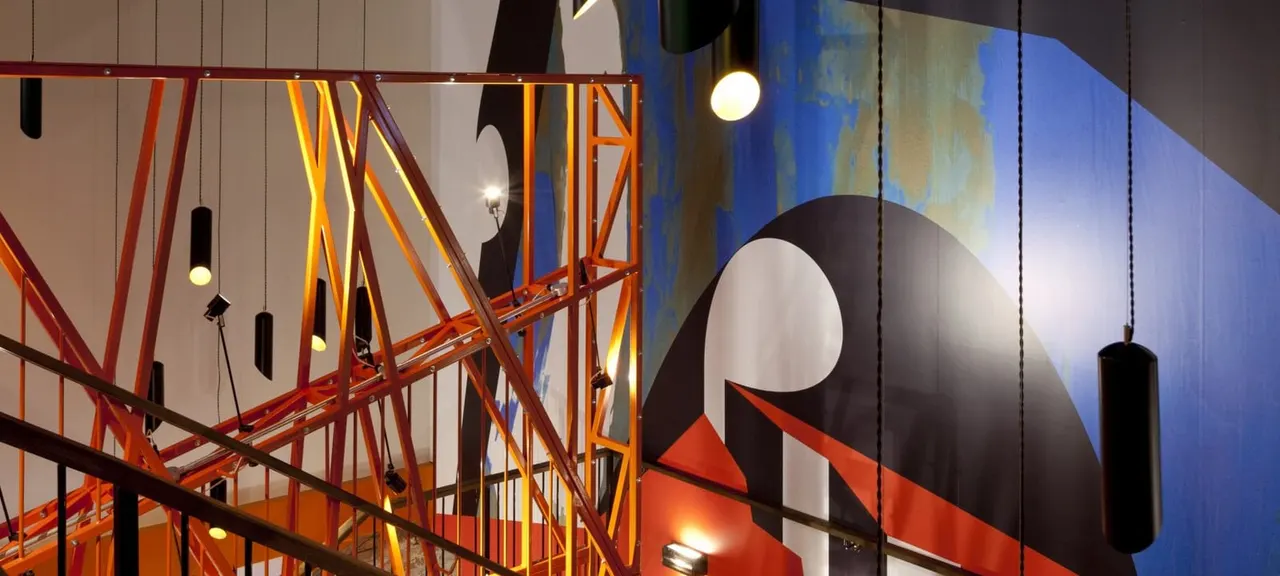Interior of a cinema with modern metal framework, pendant lighting and abstract geometric wall art in red, black and blue tones.