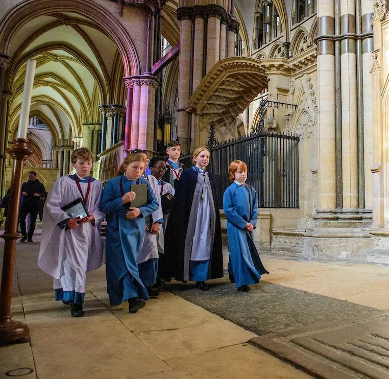 Children in historical costume walk through a Gothic cathedral nave with soaring arched ceilings and stone columns.