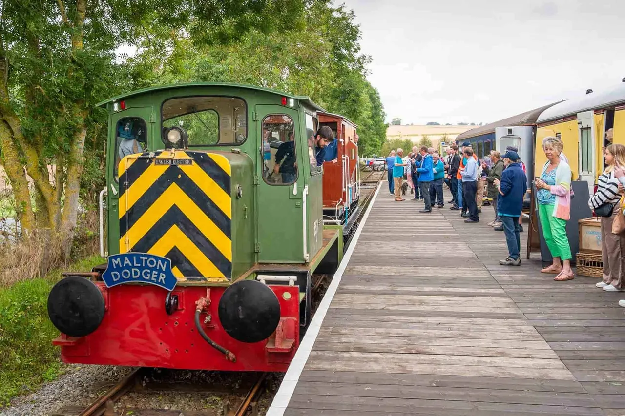 Heritage steam train with passengers boarding and standing on platform alongside vintage railway carriages.