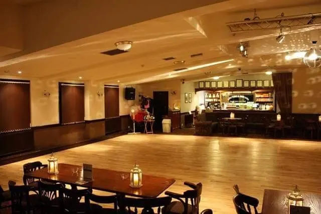 Spacious indoor dance studio with wooden floor, bar counter, seating areas and warm lighting.