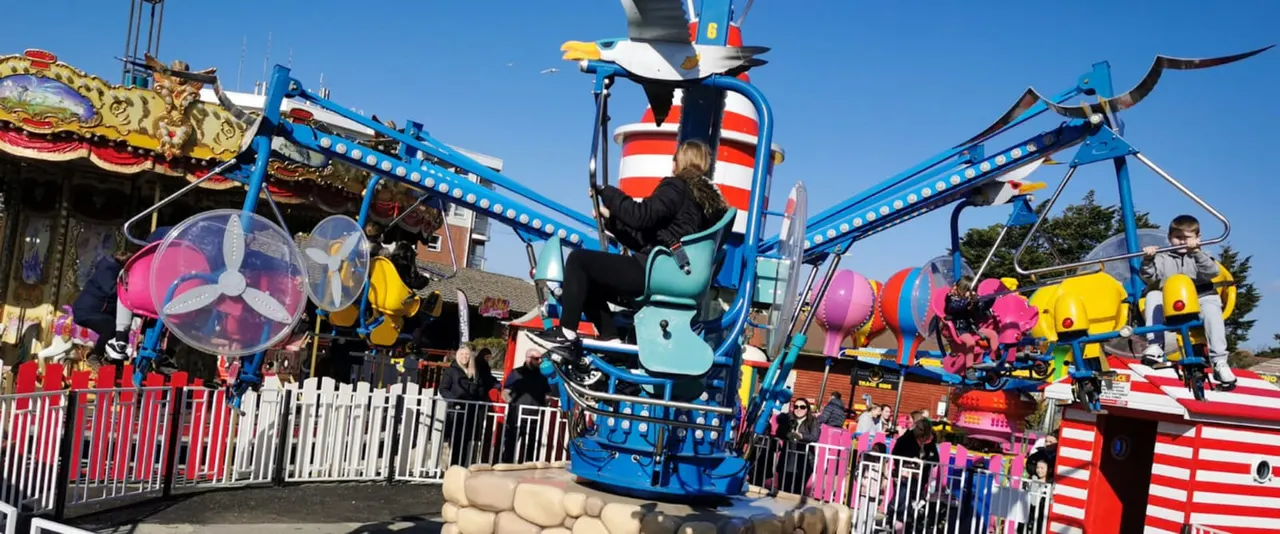 Visitor on a bright blue fairground ride with swinging arms at a busy amusement park on a clear day.
