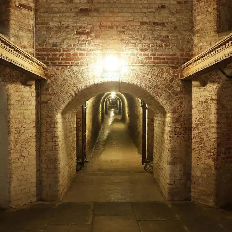 Brick-lined underground tunnel with arched ceiling and atmospheric lighting stretching into the distance.
