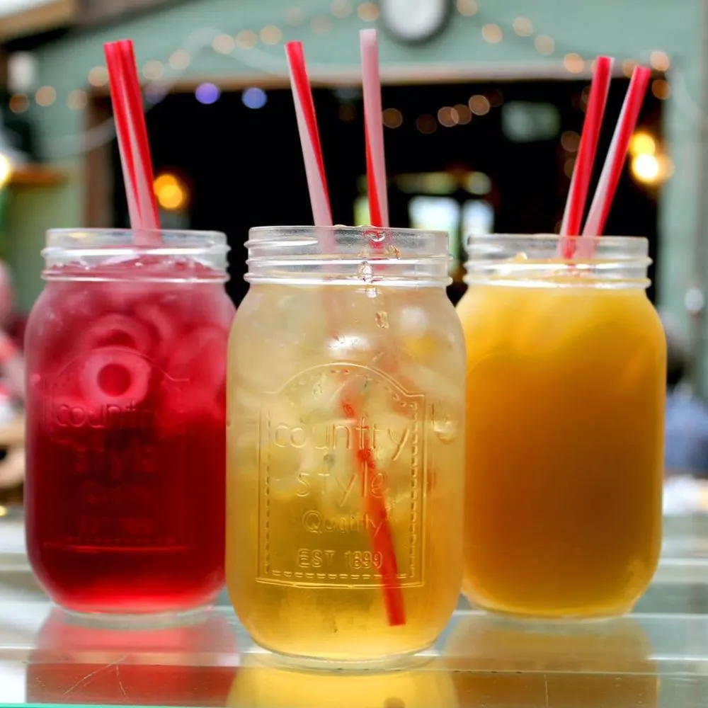 Three mason jars with coloured drinks and straws on a counter in a café.