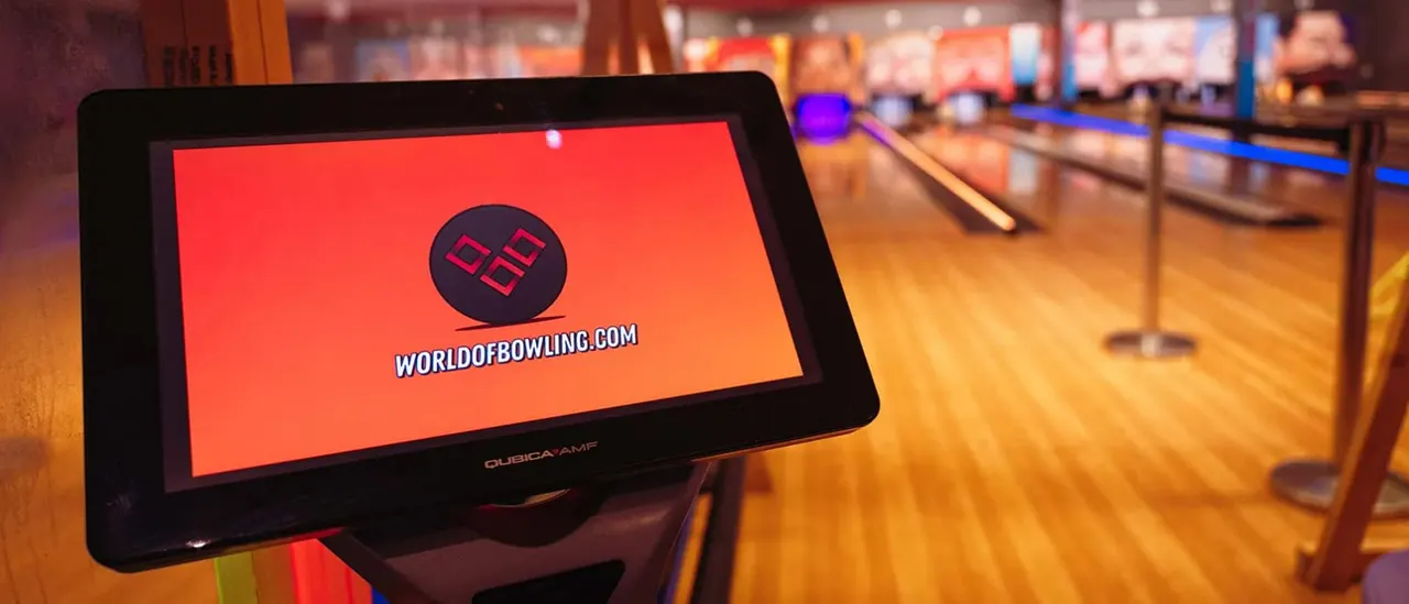 Touchscreen display showing World of Bowling logo on a lane in a bowling alley with pins and balls visible.