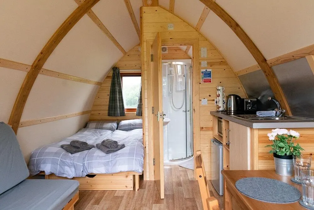 Interior of a wooden glamping pod with bed, shower room, kitchenette and seating area.