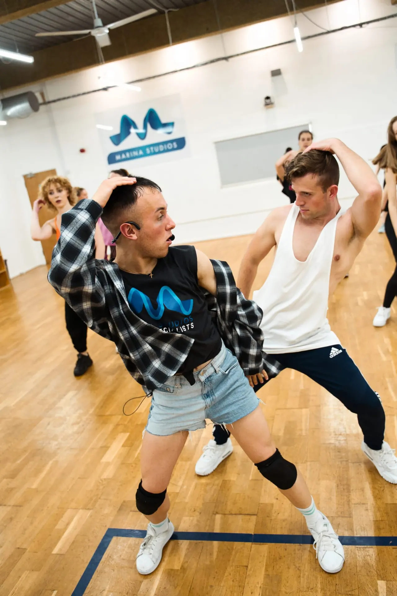 Two people dancing together in a studio with wooden floors and Marina Studios branding visible on the wall.