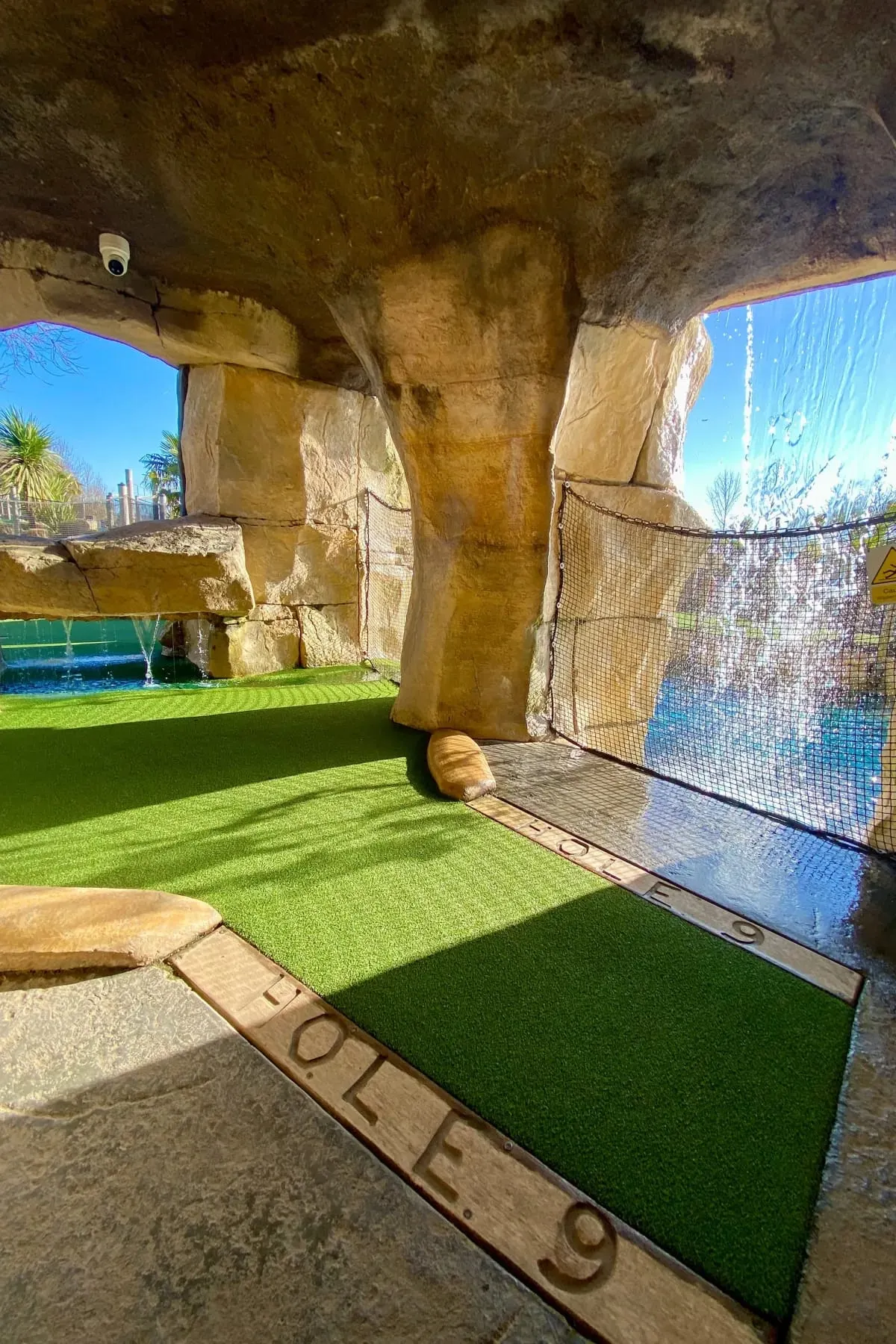 Indoor mini golf hole beneath a concrete bridge structure with artificial turf, wooden props and netting.
