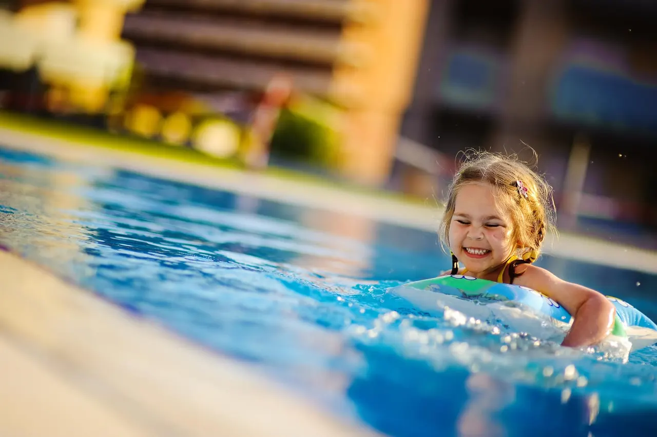 A young child smiling in a swimming pool, holding onto the edge during a swimming lesson.