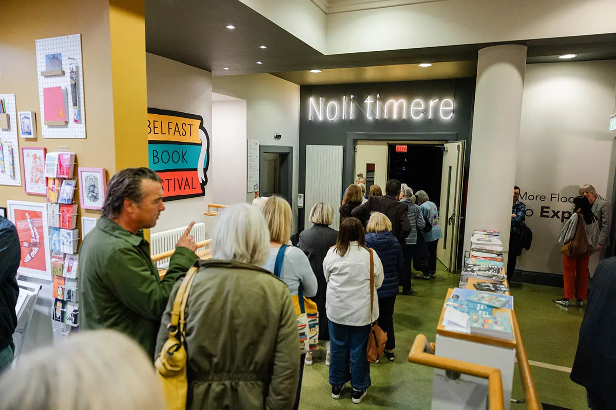 Visitors browsing and queuing inside a contemporary arts venue with colourful signage and book displays.