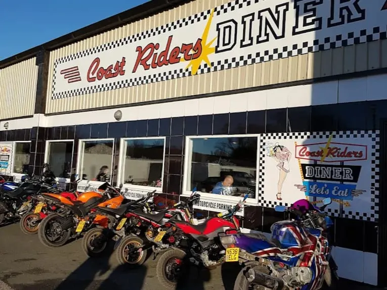 This is a photograph of the exterior of Coast Riders Diner, a themed restaurant venue, with several motorcycles and quads parked outside on a clear day.