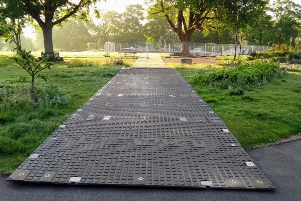 Paved pathway through park grounds with trees and sports facilities visible in the distance.