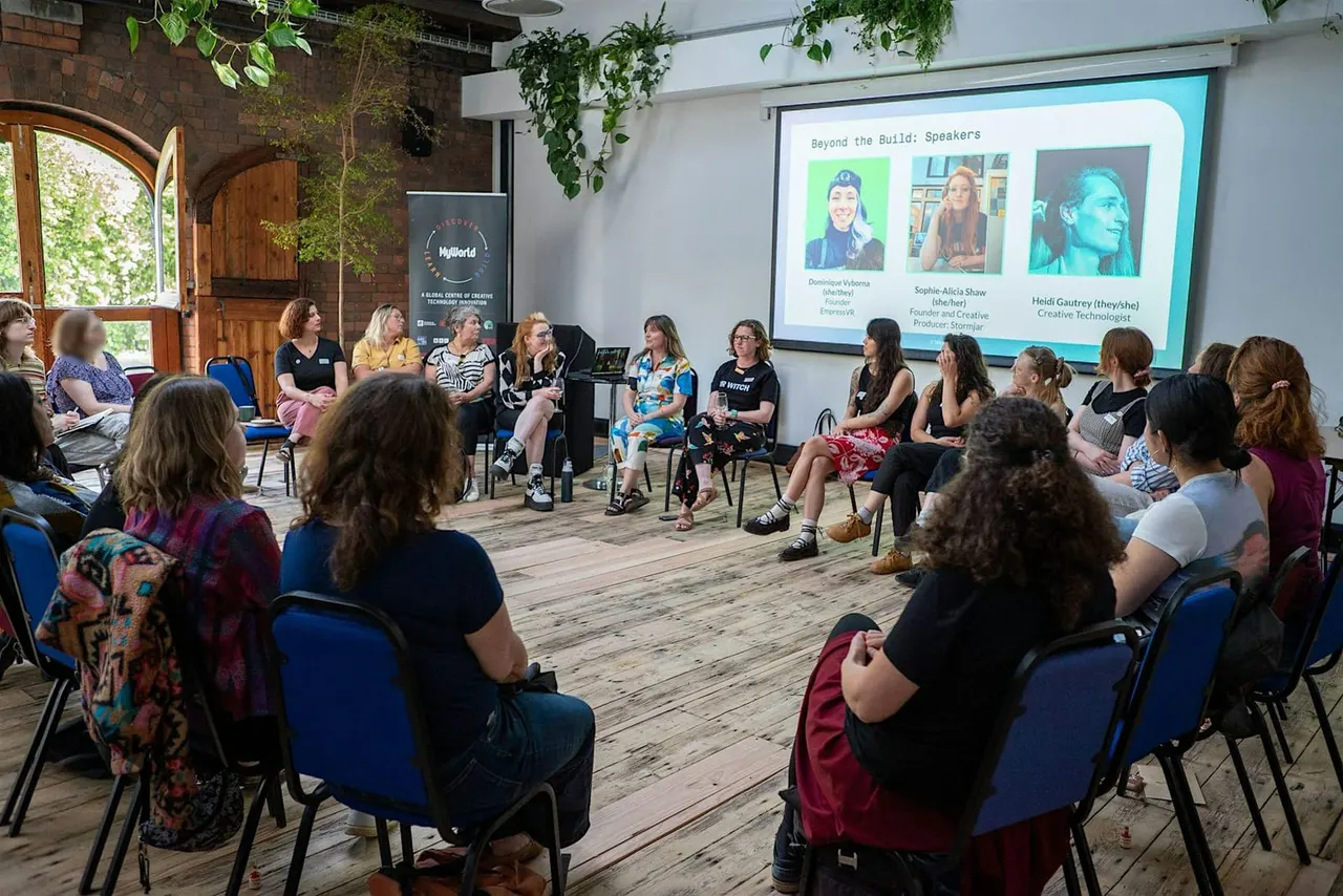 A panel discussion with women speakers seated facing an audience in a brick industrial space with hanging plants, projection screen showing speaker profiles.