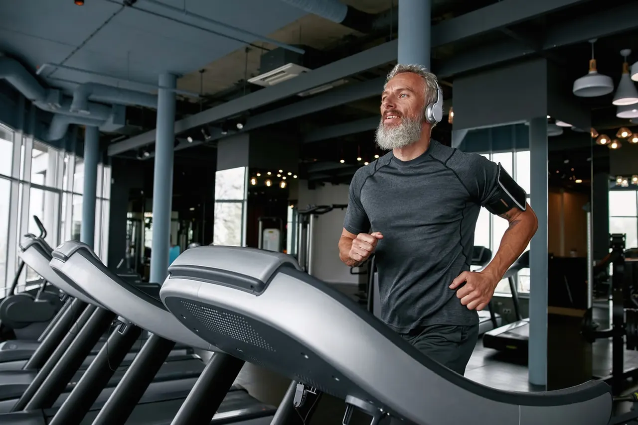 Man running on a treadmill whilst wearing headphones in a modern gym.