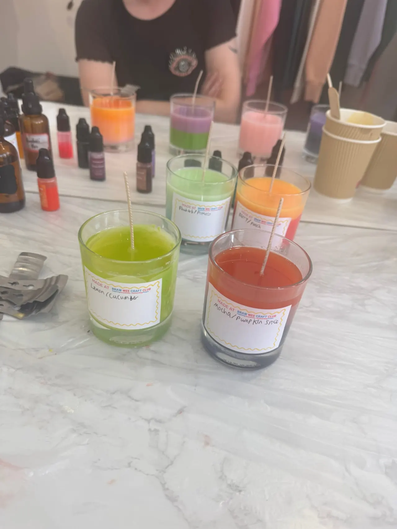People participate in a candle-making workshop, with finished scented candles in various colours displayed on a marble table.