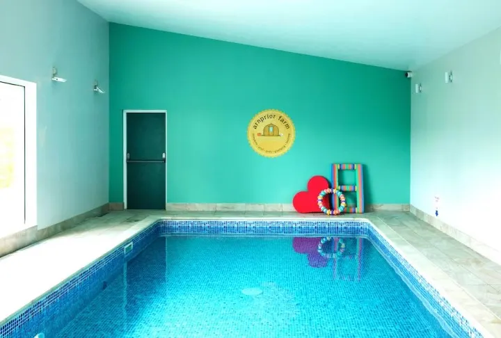 Indoor swimming pool with bright turquoise walls, blue tiled pool, and colourful play equipment beside the water.